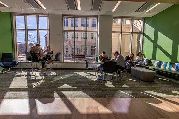 Six students read and study in a sunlight-filled study  lounge in the CHSW building - the middle wing exterior of the building can be seen through the large window