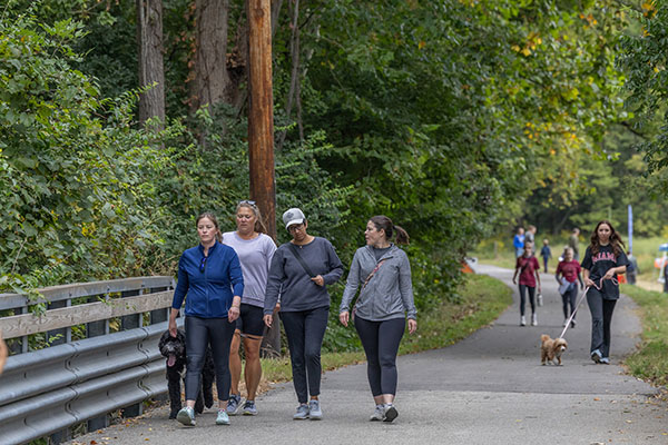 several people and a dog walk along the trail near the DeWitt Cabin in the Natural Areas during hike-a-thon