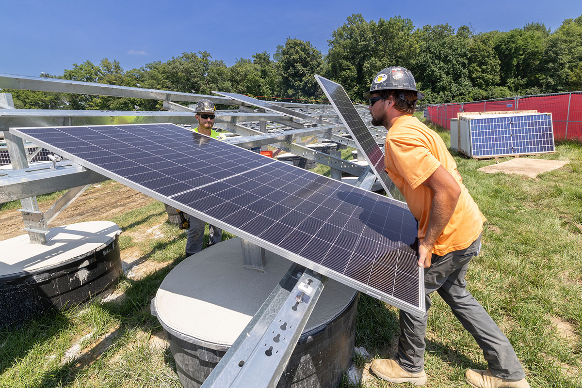 A worker lifts a solar panel onto a ground mounted rack in the western geothermal solar field